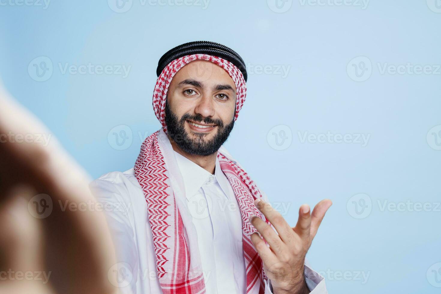 contento sorridente uomo vestito nel tradizionale musulmano Abiti chat durante video conferenza fpv. allegro arabo Tenere smartphone nel mano e guardare a telecamera primo persona Visualizza foto