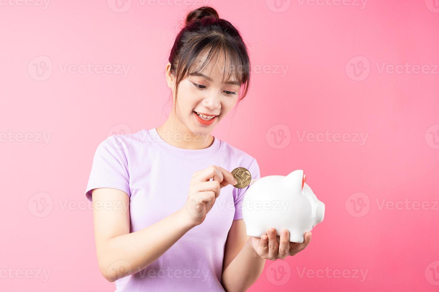 ritratto di ragazza che conia soldi nel maiale, isolato su sfondo rosa foto