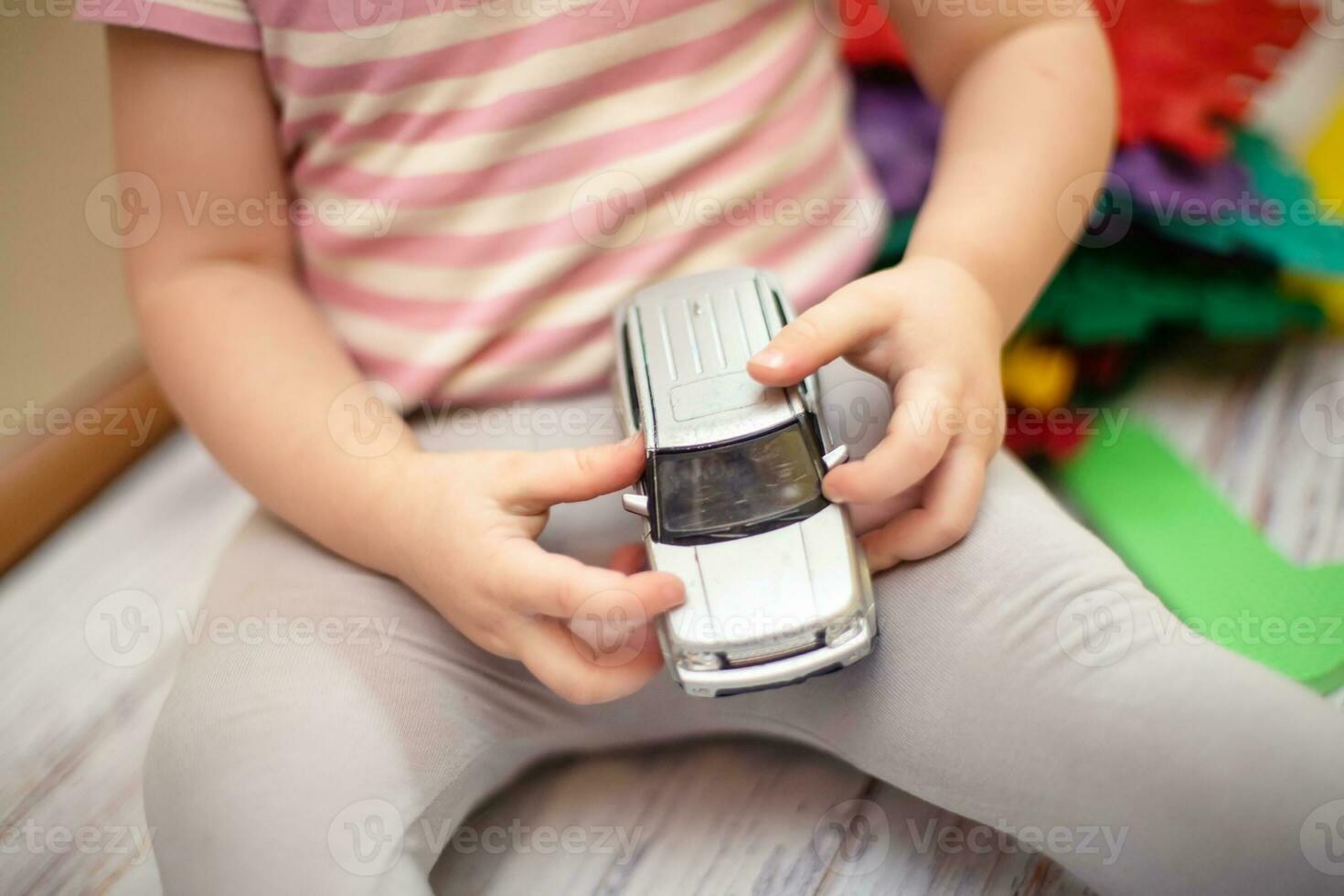 del bambino mani Tenere macchina. piccolo bambino giochi a casa su pavimento di giocattolo modello minivan foto