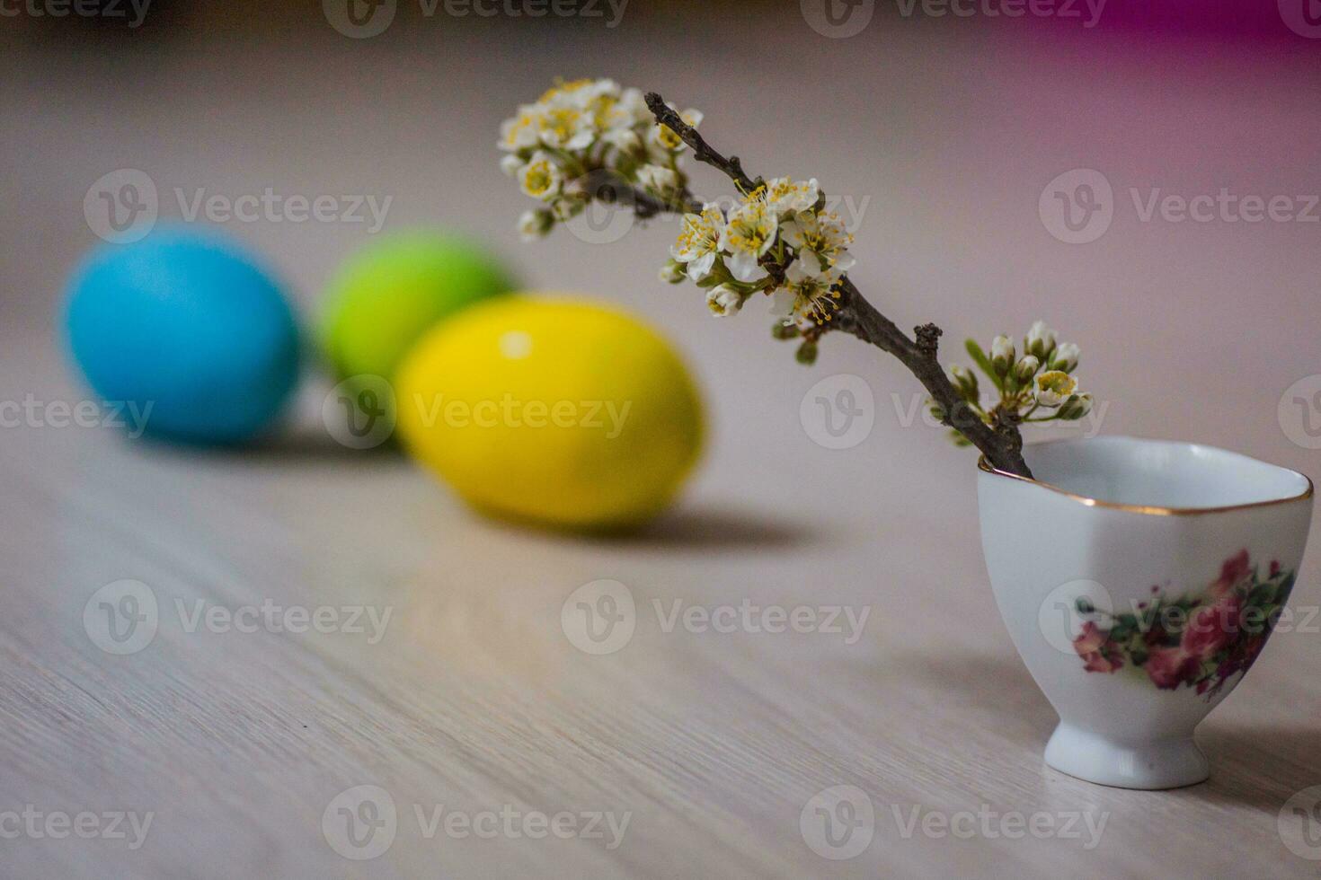 tre Pasqua uova vicino un' tazza con un' rametto di prugna. Pasqua sfondo per mobile e computer schermi. foto
