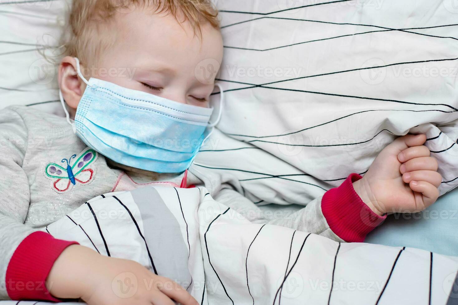 poco bambino dorme nel letto nel protettivo medico maschera. malato bambino nel bianca letto. ragazzo bambino piccolo uno anni vecchio con influenza, influenza o freddo protetta a partire dal virus, inquinamento tra pazienti con coronavirus foto