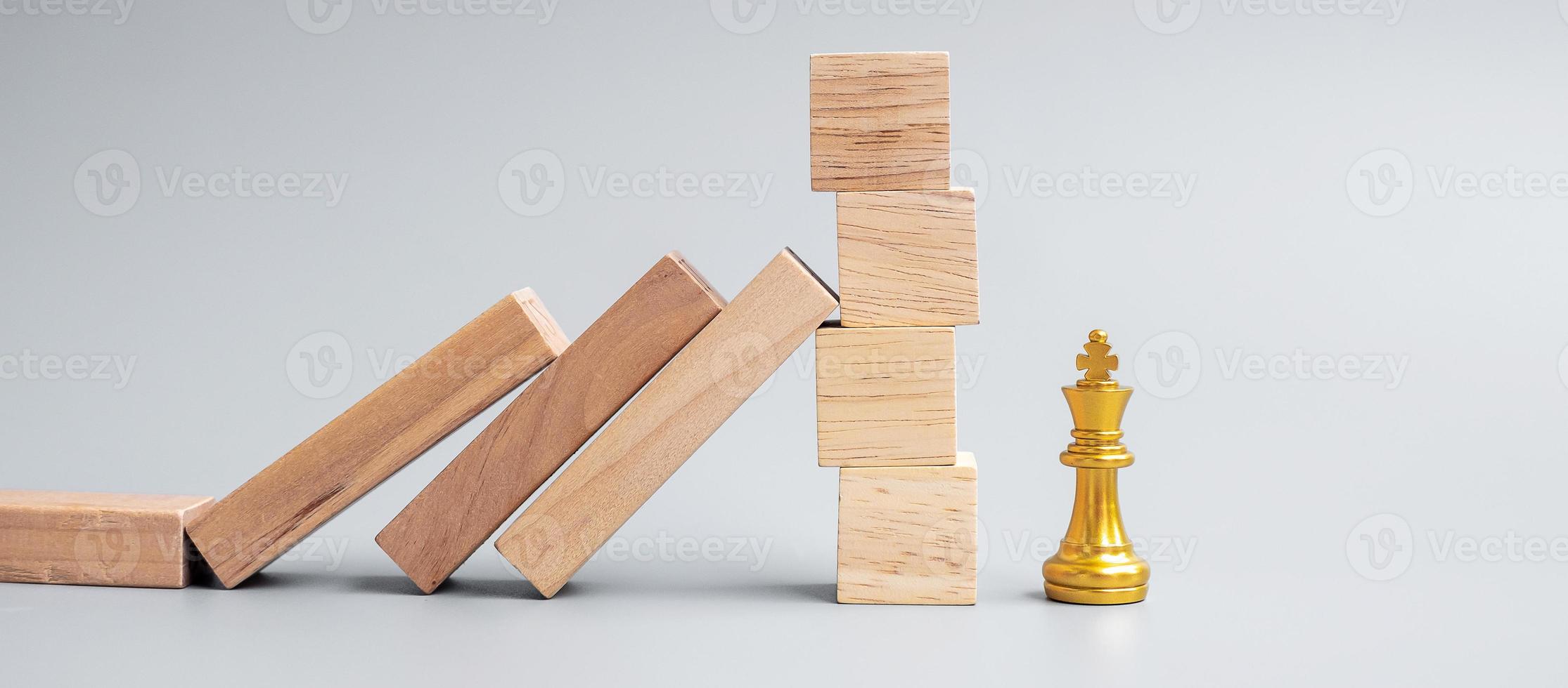 blocchi di legno o domino che cadono sulla figura del re degli scacchi d'oro. affari, gestione del rischio, soluzione, regressione economica, assicurazione foto