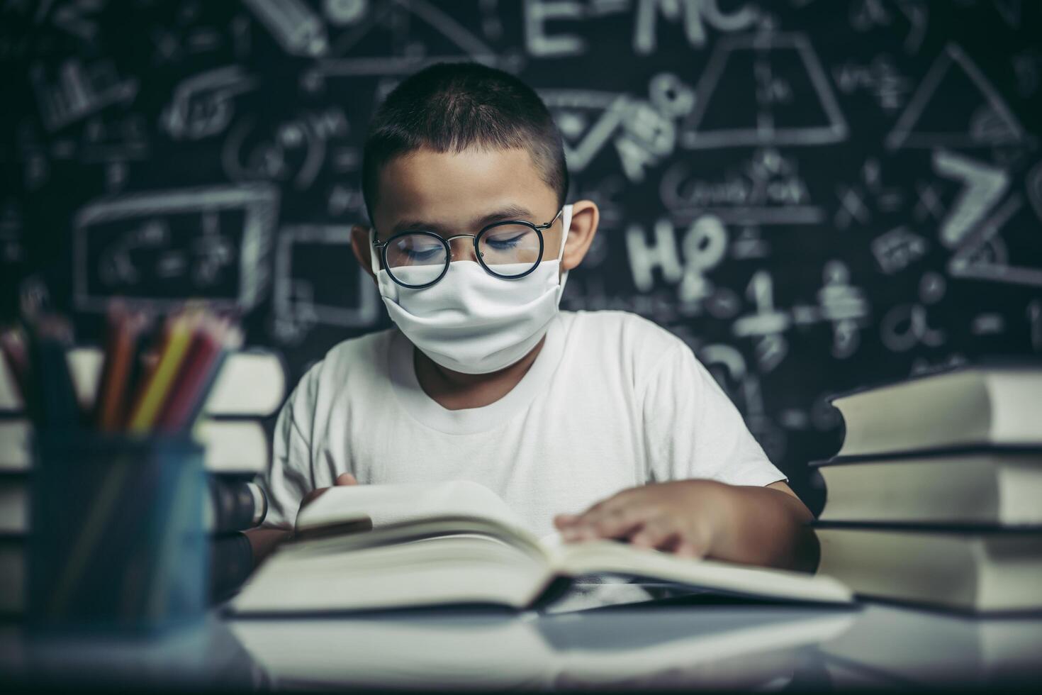 un ragazzo con gli occhiali seduto in classe a leggere foto