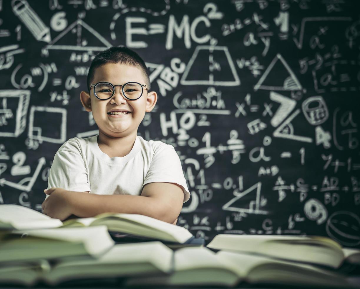 un ragazzo con gli occhiali seduto in classe a leggere foto