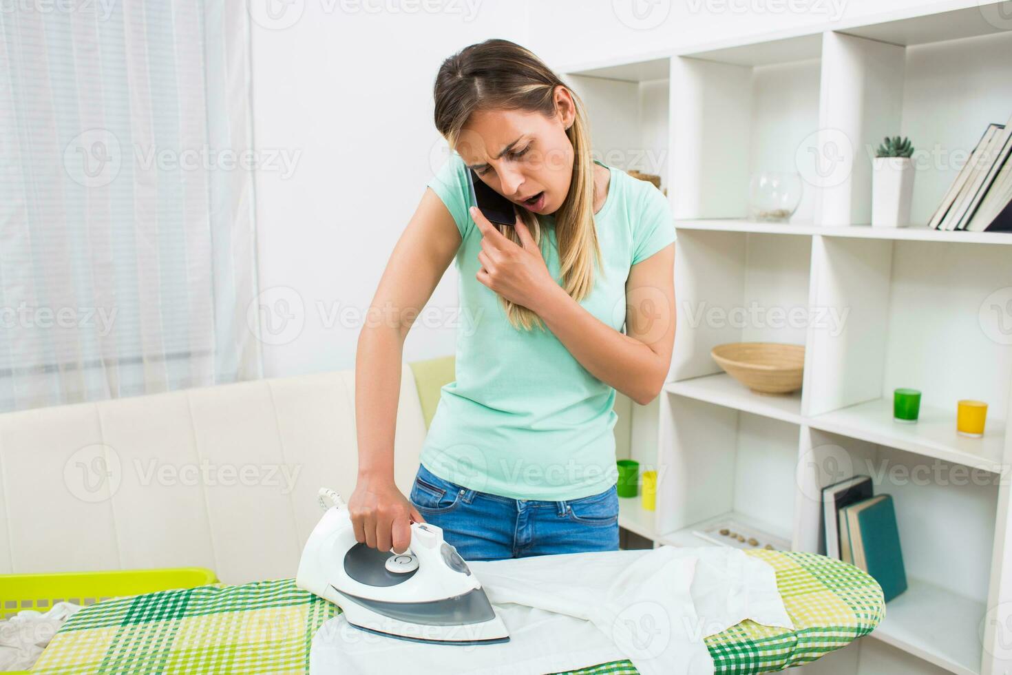 occupato e preoccupato donna parlando su il Telefono e Stirare a il stesso tempo foto