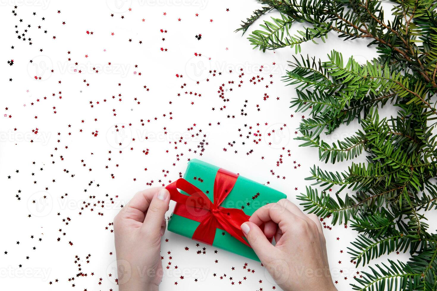 mani hold uno Natale regalo con rosso nastro su il bianca tavolo con Natale albero nelle vicinanze . Natale involucro foto
