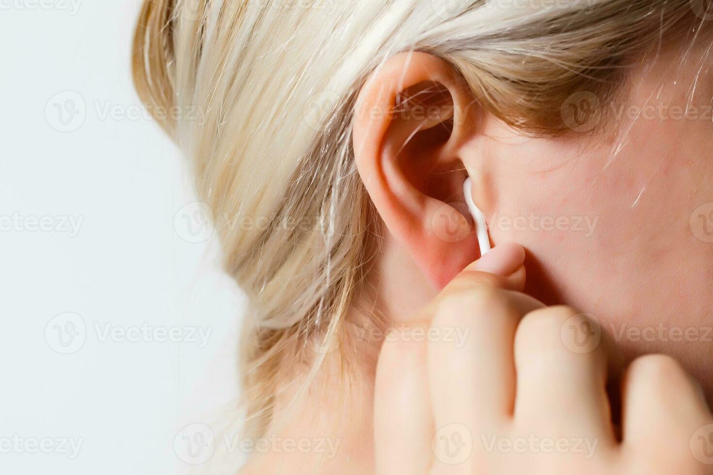 bionda donna pulisce sua orecchio con un' bianca cotone tampone vicino su foto