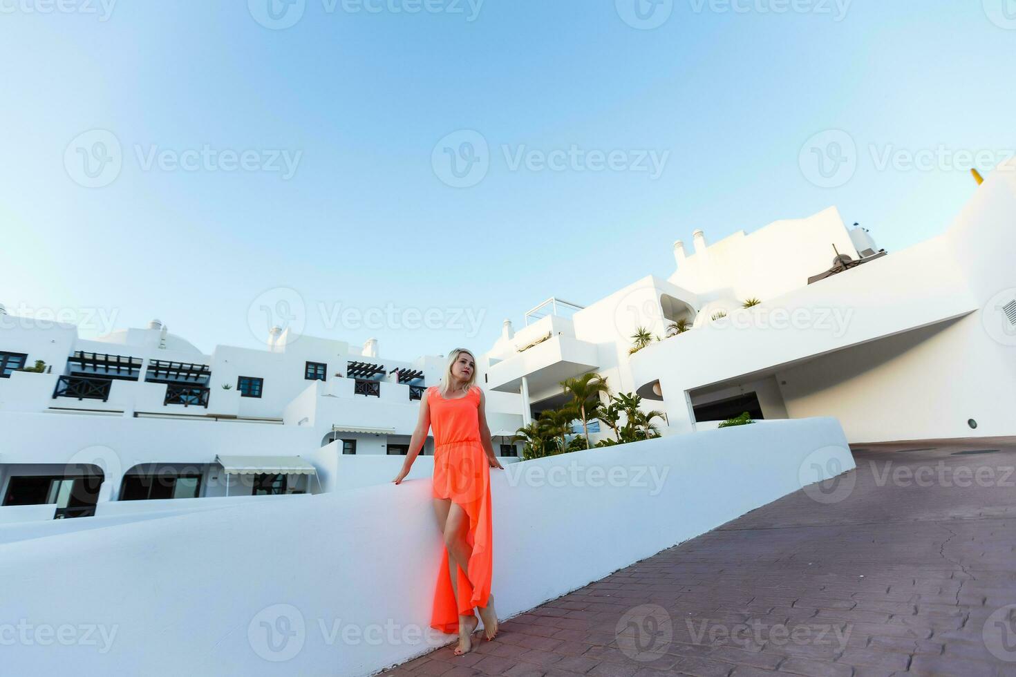 elegante giovane attraente donna vestito nel un color arancio fotografato nel il estate su un' sfondo di palma alberi foto