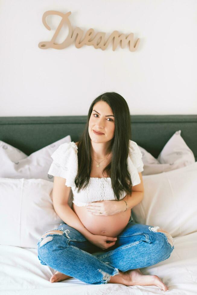 interno ritratto di bellissimo giovane incinta donna riposo su letto foto