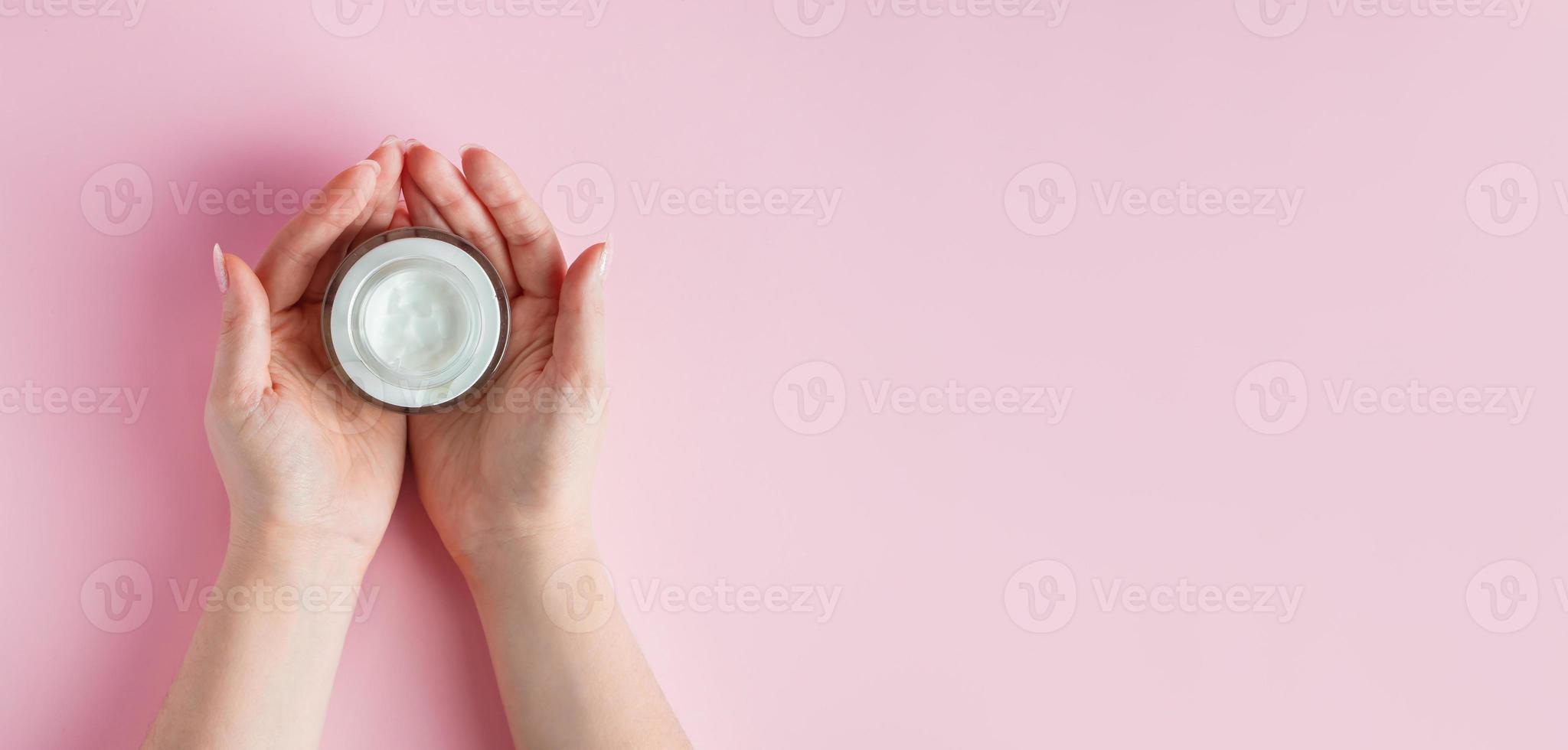 mani femminili con una bottiglia di crema su sfondo rosa. concetto di spa e cura del corpo. immagine per la pubblicità. foto