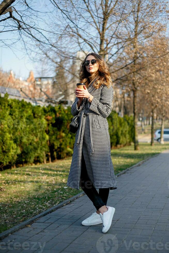 donna nel trincea cappotto a piedi e potabile caffè a partire dal carta tazza foto