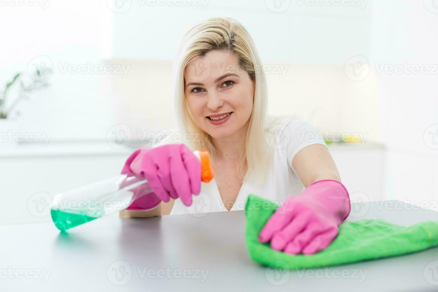 pulizia è nel tendenza. bella sorridente donna asciugandosi tavolo con stoffa e speciale si intende di lavaggio foto