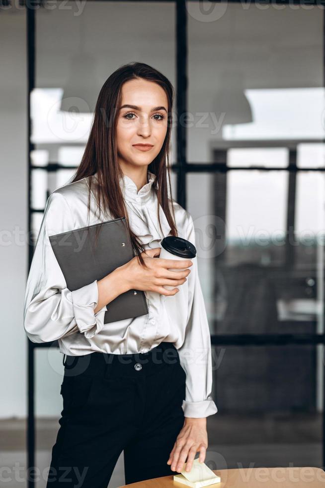 bella mora con documenti in lei e tazze di caffè, lavorando nell'ufficiale foto