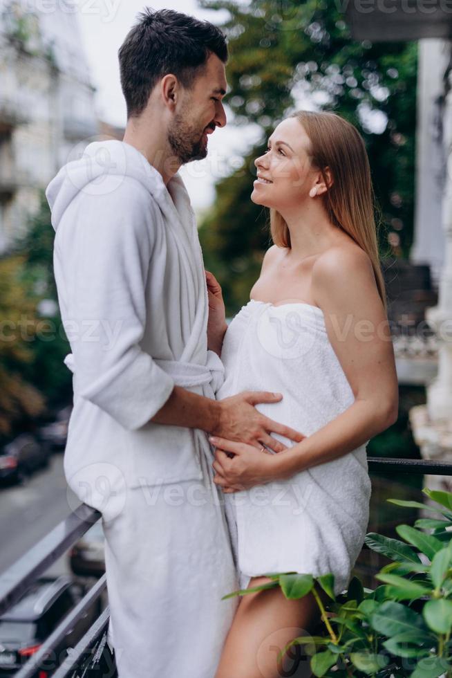 donna incinta avvolta in un asciugamano sul balcone con il marito foto