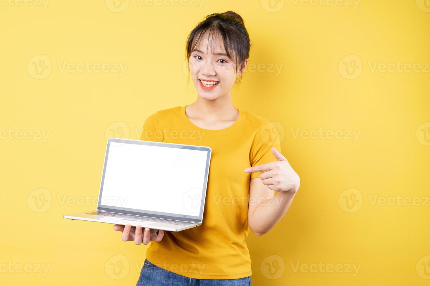 Ritratto di giovane ragazza con laptop in mano su sfondo giallo foto
