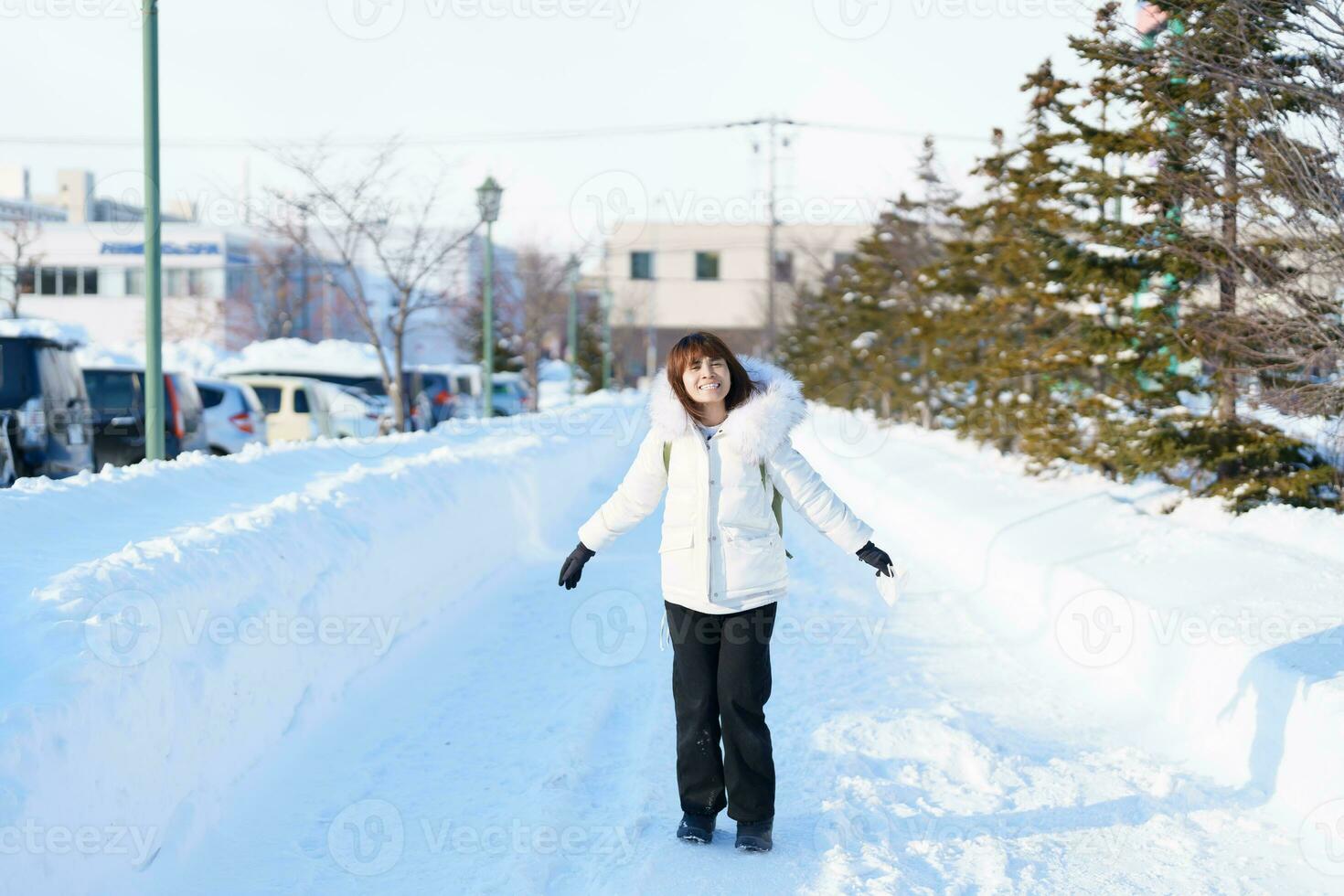 contento viaggiatore con maglione e zaino a piedi su neve coperto strada nel gelido tempo atmosferico, donna turista giro turistico nel sapporo città, hokkaido, Giappone inverno viaggio e vacanza concetto foto