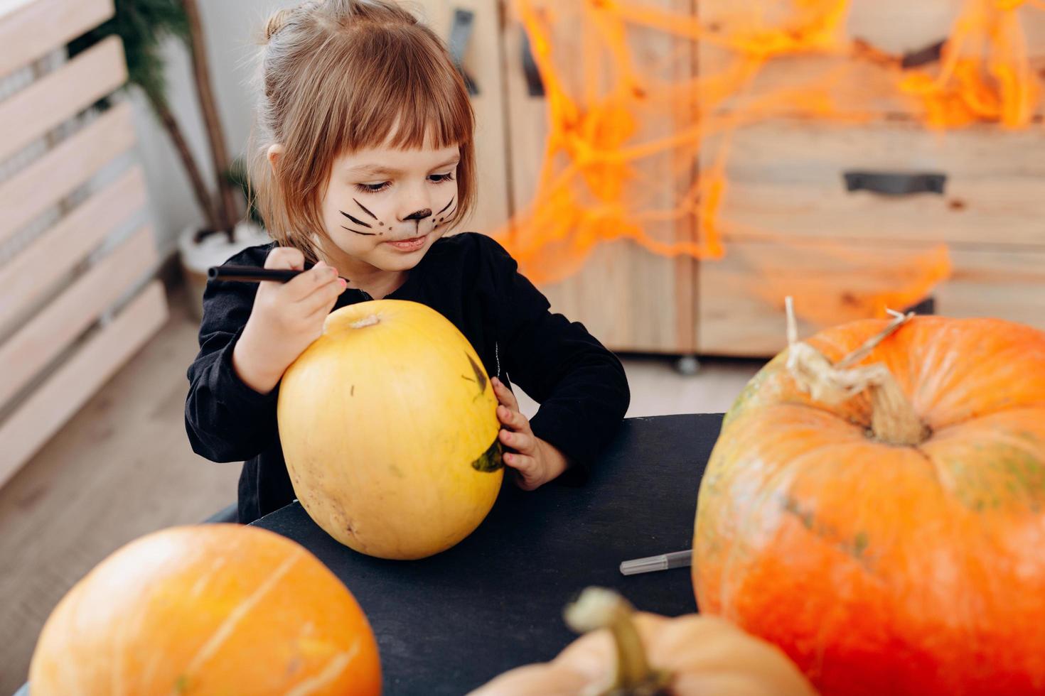 bambina disegno su zucca seduta al tavolo. - Immagine foto