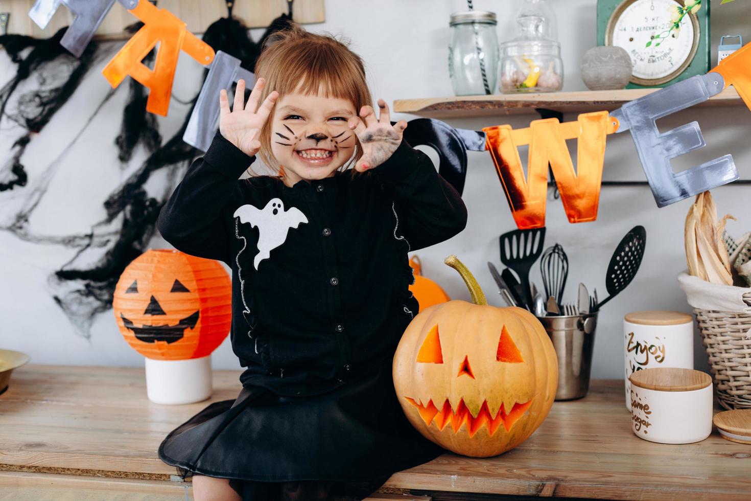piccola ragazza divertente seduta accanto alla zucca e mostrando un gesto spaventoso. - concetto di halloween foto