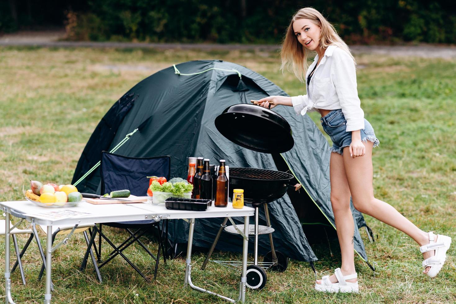 donna che prepara il cibo sul barbecue all'aperto nel campeggio e guarda la telecamera foto