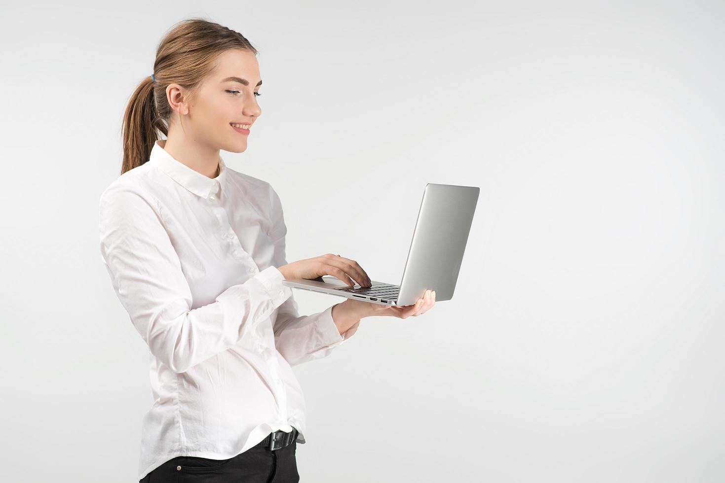 donna d'affari sorridente in camicia bianca che tiene il computer portatile e lavora stando in piedi foto