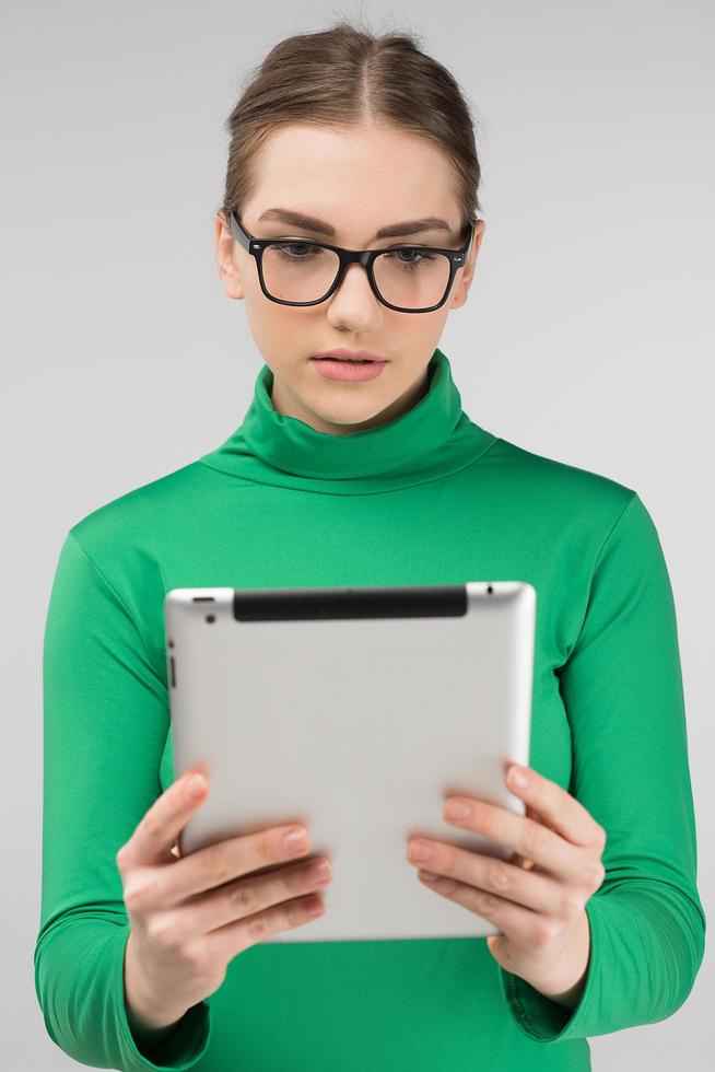 ragazza con gli occhiali che tiene un tablet in mano e guarda seriamente foto