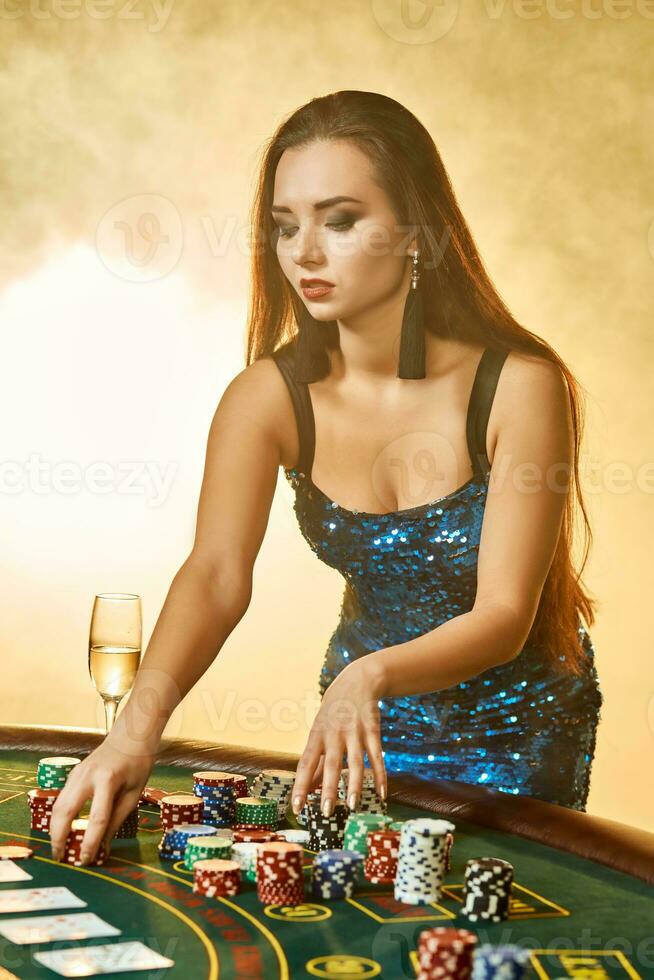 giovane bellissimo donna pose vicino poker tavolo nel lusso casinò. passione, carte, patatine fritte, alcol, dado, gioco d'azzardo, casinò - esso è come femmina intrattenimento. Fumo sfondo. foto