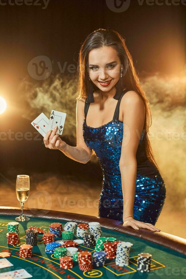 giovane bellissimo donna pose vicino poker tavolo nel lusso casinò. passione, carte, patatine fritte, alcol, dado, gioco d'azzardo, casinò - esso è come femmina intrattenimento. Fumo sfondo. foto