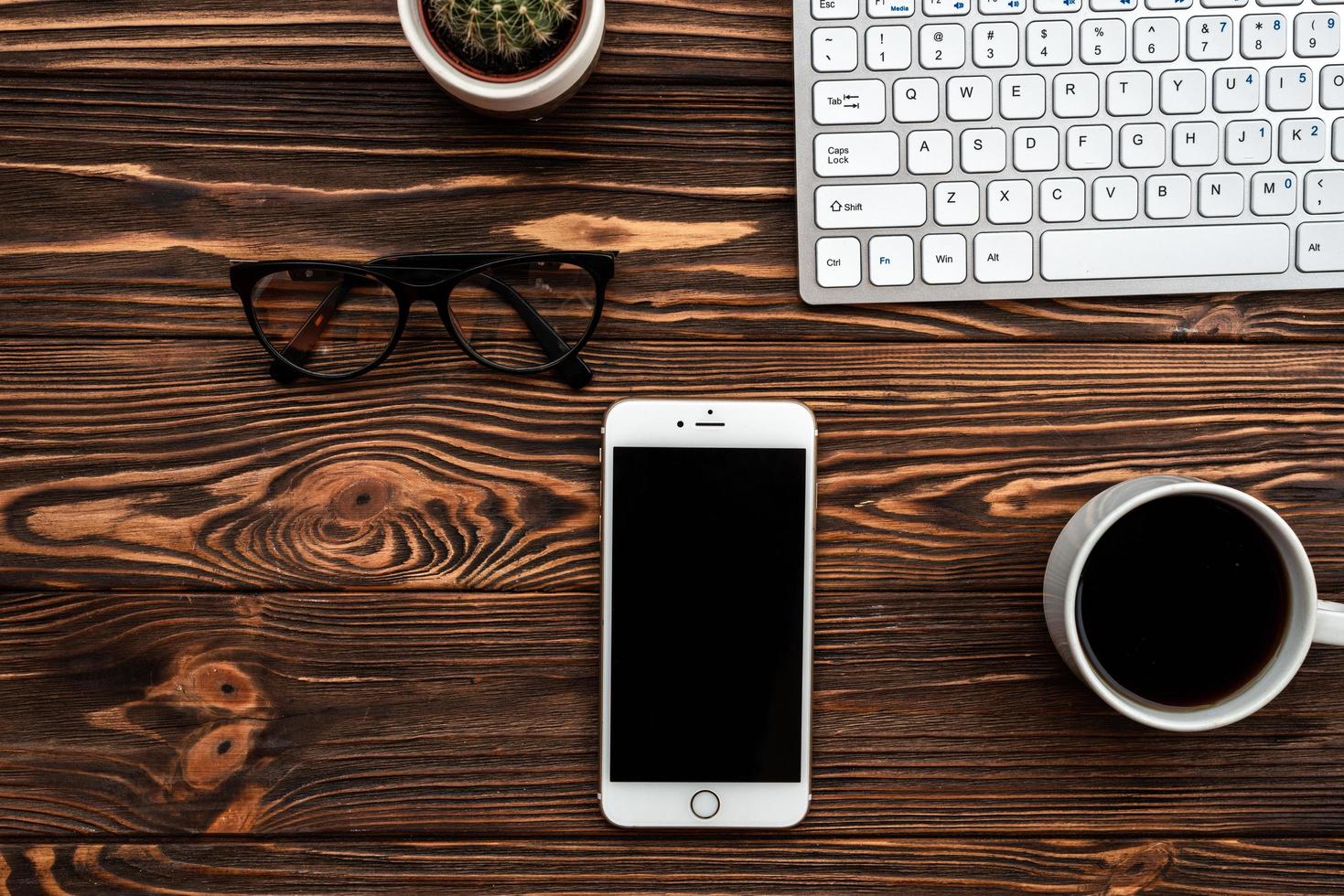 scrivania da ufficio vista dall'alto con una tazza di caffè e smartphone e occhiali foto