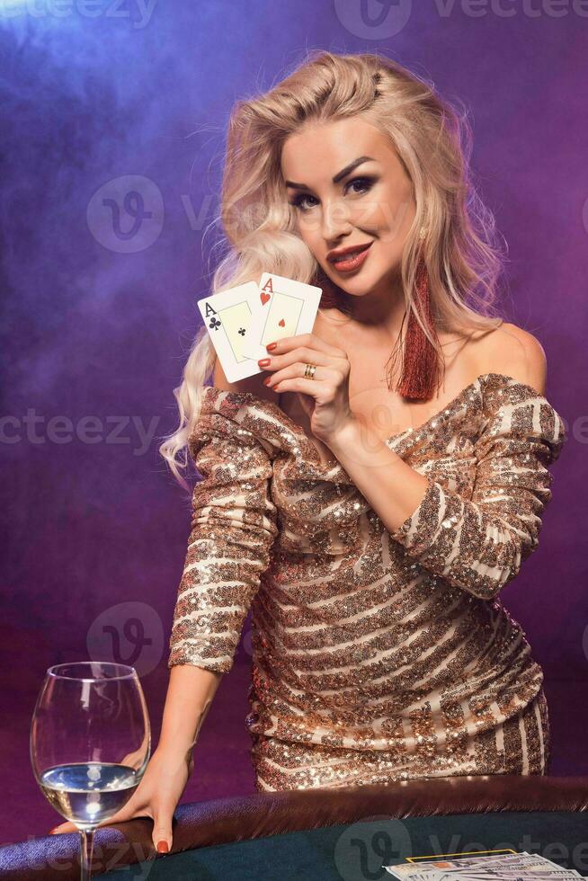 bionda donna con un' Perfetto acconciatura e luminosa trucco è in posa con giocando carte nel sua mani. casinò, poker. foto