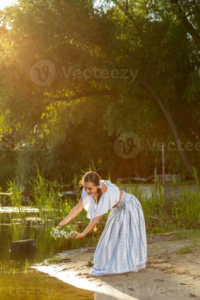 giovane bellissimo caucasico donna in piedi a il banca di fiume. tradizionale campagna immagine con ragazza a primo piano e copia spazio. sole bagliore foto