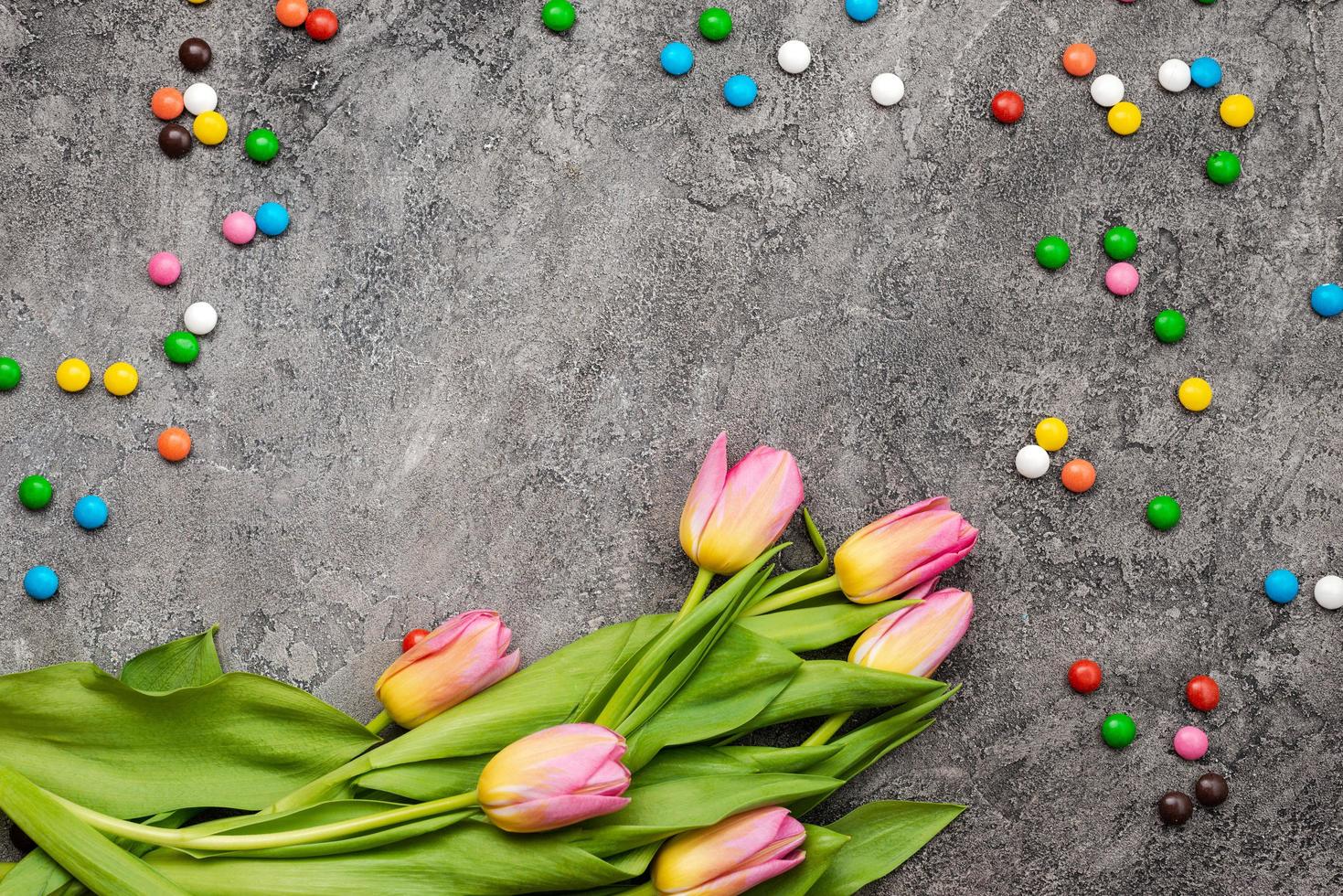 sfondo di pasqua con caramelle multicolori e tulipani su uno sfondo di gesso grigio foto