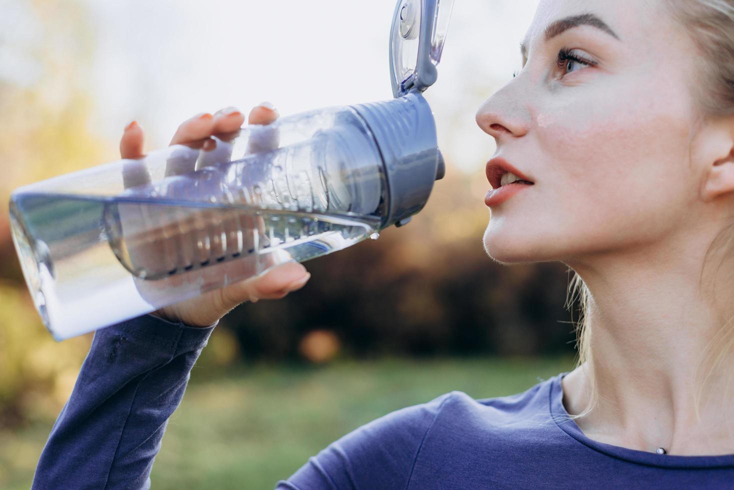 fitness nel parco, ragazza beve acqua da una bottiglia, primo piano. foto