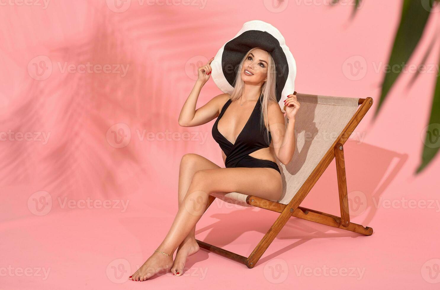 giovane donna nel nero costume da bagno rilassante su carrozza longue, studio sparo. sfocato palma albero le foglie nel primo piano. foto