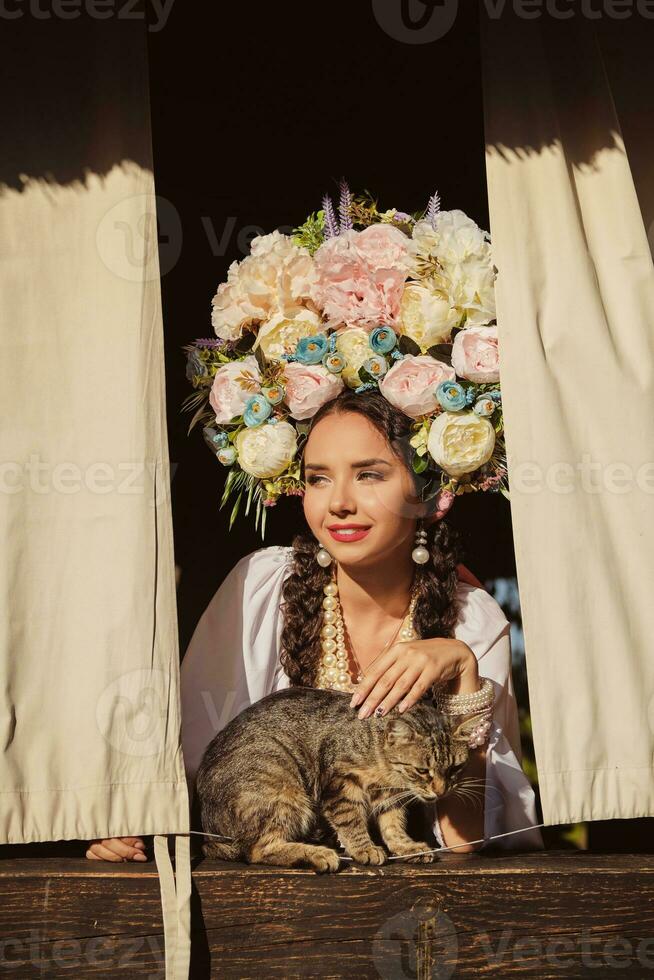 brunetta ragazza nel un' bianca ucraino autentico nazionale costume e un' ghirlanda di fiori è è guardare su di il finestra. avvicinamento. foto