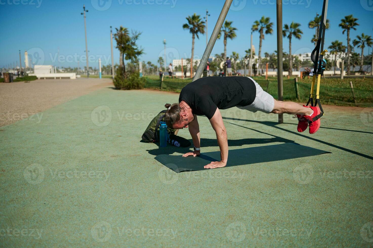 giovane adulto sportivo fare scricchiolii mentre esercizio con sospensione cinghie su all'aperto campo sportivo foto