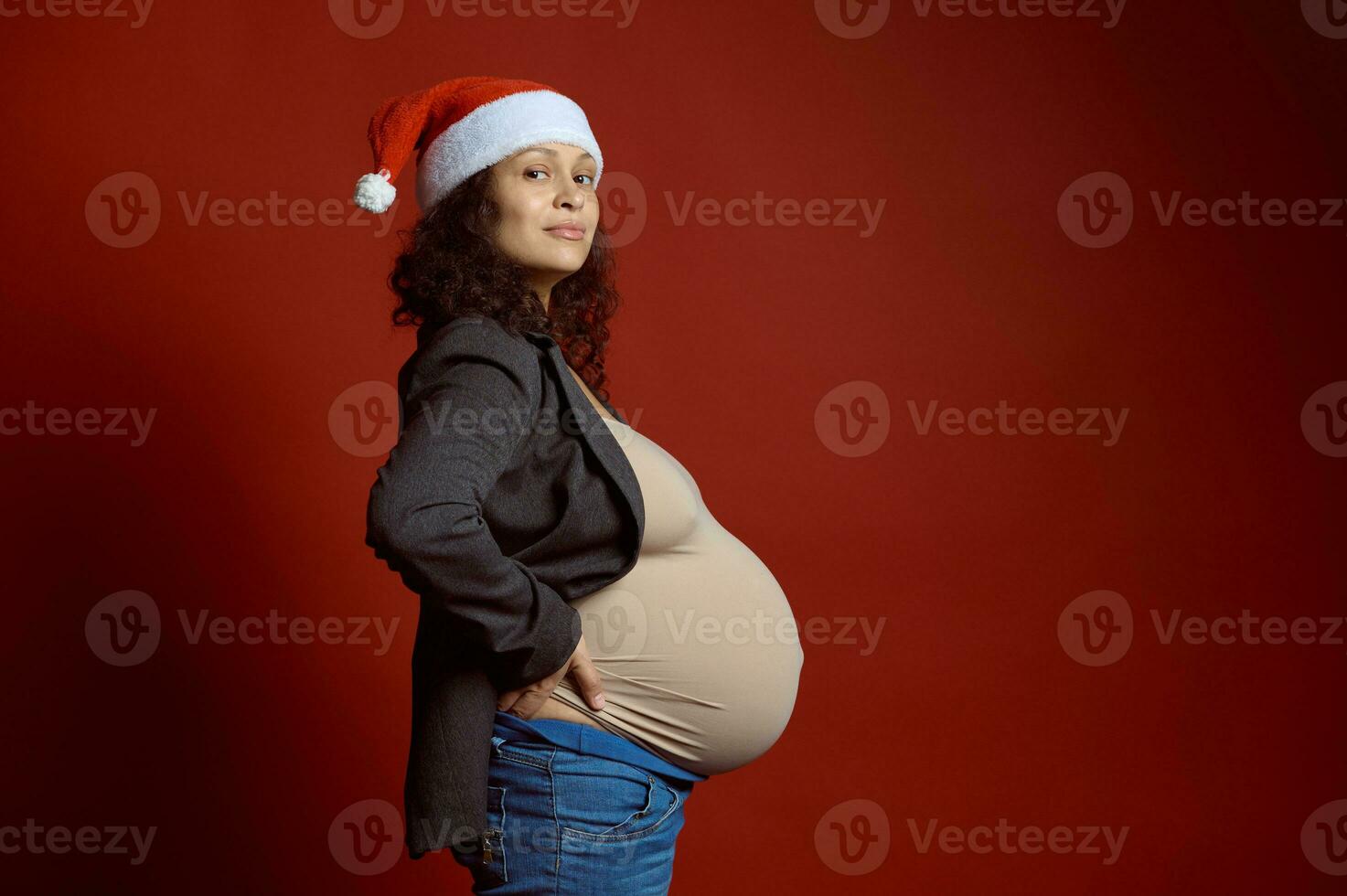 lato ritratto bella incinta donna nel Santa cappello, mostrando sua grande pancia nel gravidanza terzo trimestre, sorrisi a telecamera foto