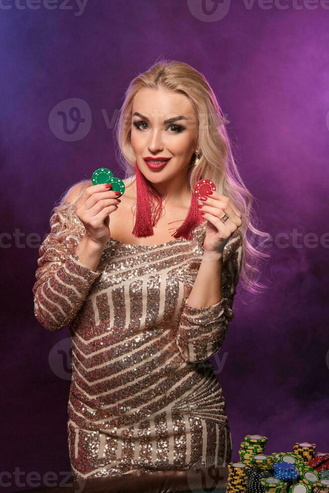 bionda donna con un' Perfetto acconciatura e luminosa trucco è in posa con gioco d'azzardo patatine fritte nel sua mani. casinò, poker. foto