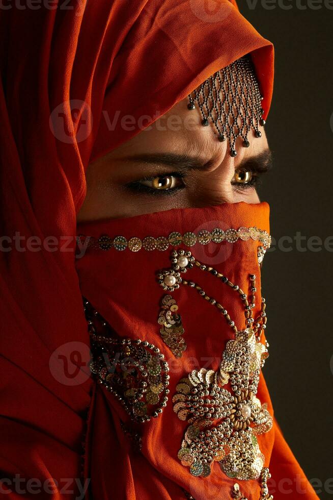 studio tiro di un' giovane affascinante donna indossare il terracotta hijab decorato con paillettes e gioielleria. Arabo stile. foto