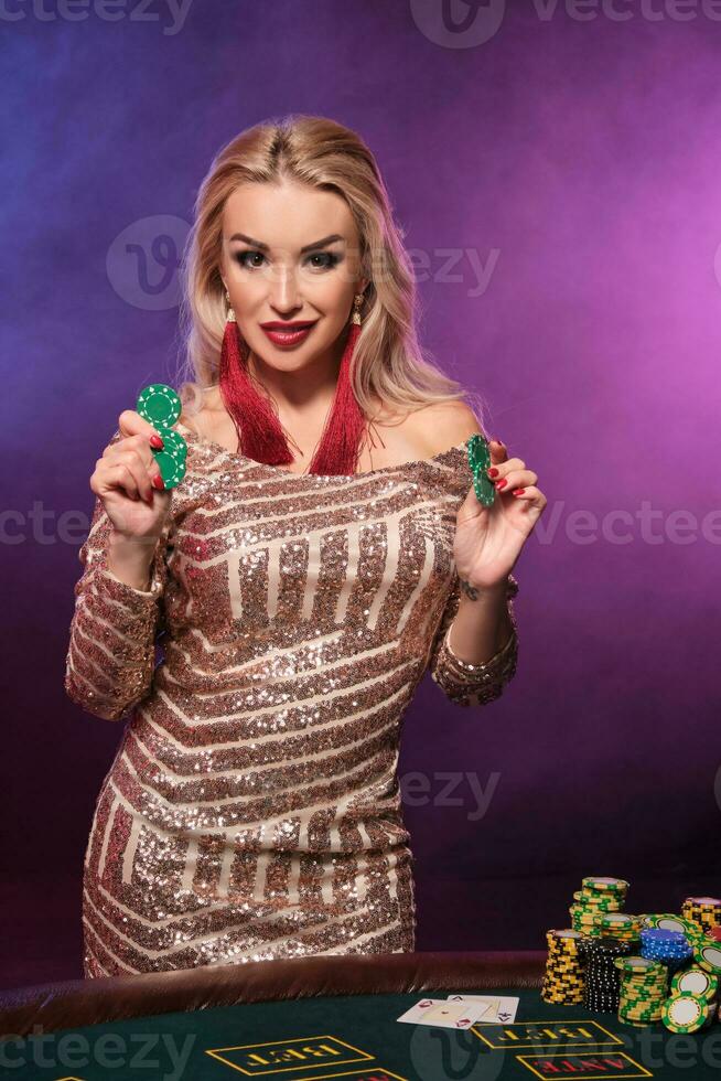 bionda donna con un' Perfetto acconciatura e luminosa trucco è in posa con gioco d'azzardo patatine fritte nel sua mani. casinò, poker. foto
