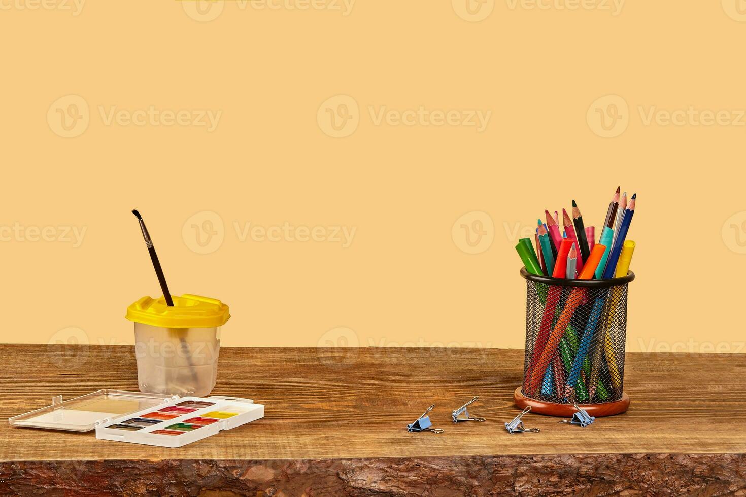 acquerello impostare, pennello, raccoglitore clip, pennarello penne e colorato matite nel In piedi su di legno del desktop contro beige sfondo. vicino su, copia spazio foto