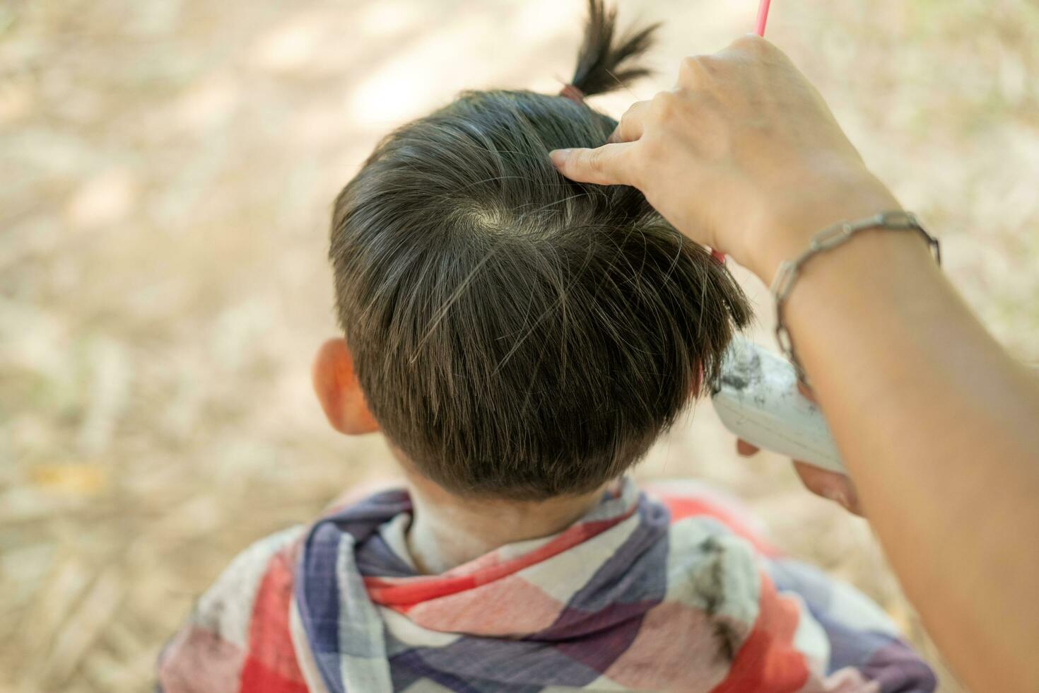 barbiere taglio capelli di un asiatico ragazzo nel un Aperto spazio pieno con alberi. foto