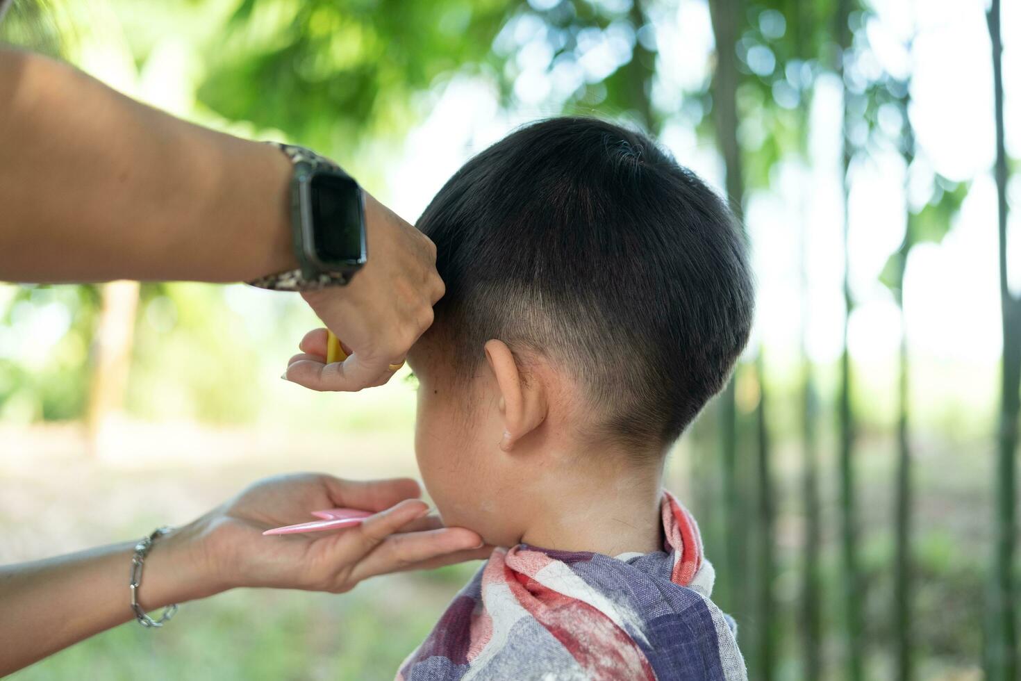 barbiere taglio capelli di un asiatico ragazzo nel un Aperto spazio pieno con alberi. foto