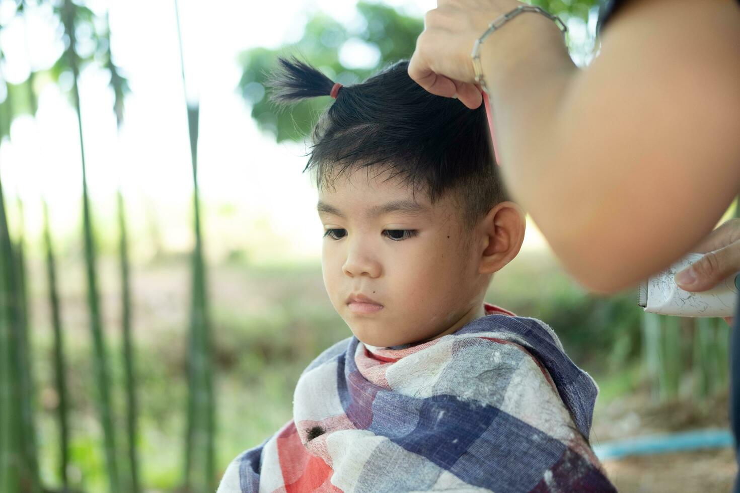 barbiere taglio capelli di un asiatico ragazzo nel un Aperto spazio pieno con alberi. foto