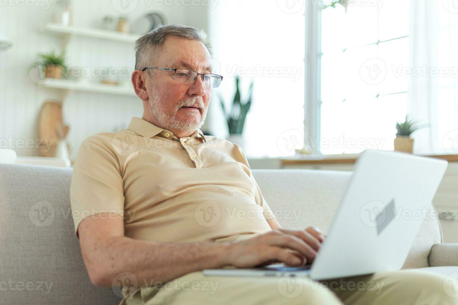 fiducioso elegante contento mezzo anziano anziano uomo utilizzando il computer portatile a casa. elegante più vecchio maturo 60s barba nonno seduta a divano guardare a computer schermo digitando chat lettura scrittura e-mail. foto
