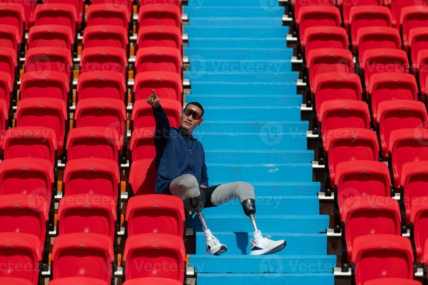 Disabilitato atleti nel un' blu camicia seduta su il rosso posti a sedere a il stadio, preparare per in esecuzione addestramento. foto