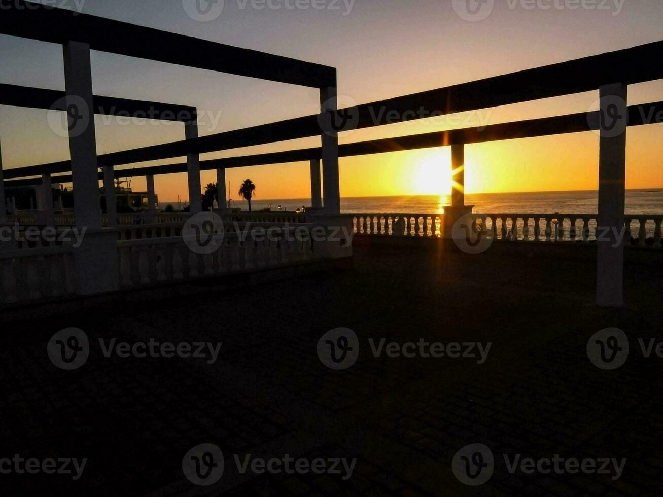 il sole ambientazione al di sopra di il oceano nel davanti di un' molo foto