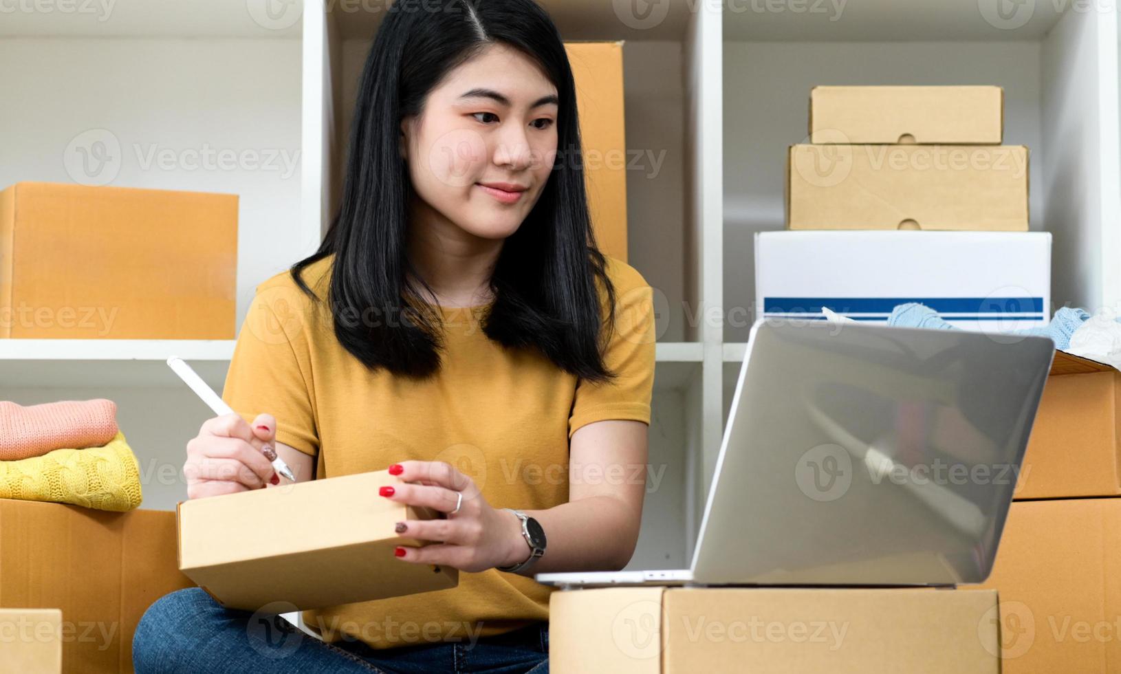 donna che guarda lo schermo del laptop e scrive l'indirizzo sulla cassetta dei pacchi, vendita online, consegna pacchi. foto