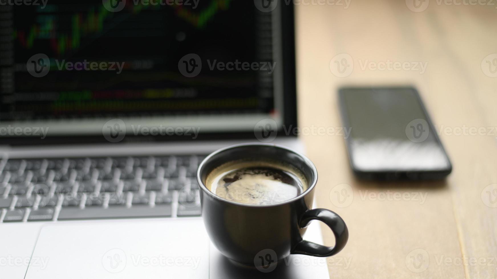 tazza da caffè posizionata sul laptop con grafico azionario sullo schermo, ripresa dalla parte anteriore. foto