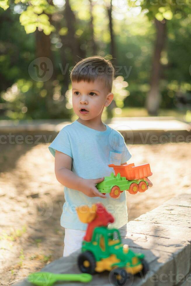 poco bambino giocando con giocattoli nel il parco su un' soleggiato giorno foto