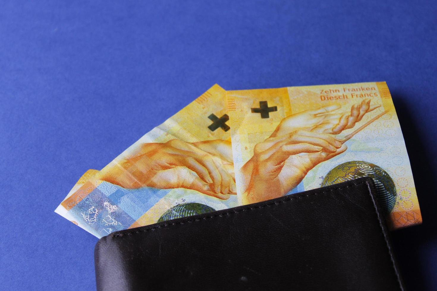 banconote svizzere di dieci franchi e portafoglio in pelle marrone su sfondo blu foto